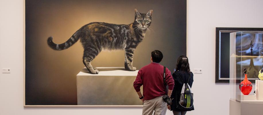 A couple looking at the  painting of the cat, Emily, in the Sonia and Isaac Luski gallery